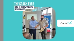 how to improve business performance: A business coach smiling and shaking hands with a client who holds a certificate in a bright workshop room