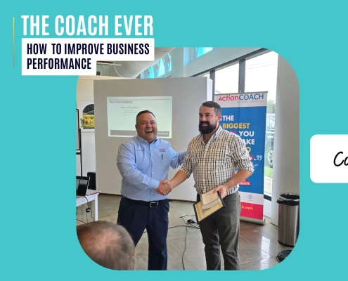 how to improve business performance: A business coach smiling and shaking hands with a client who holds a certificate in a bright workshop room