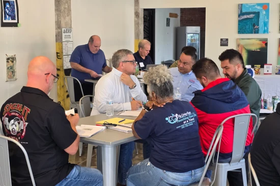 About us: Small-business owners collaborating at a table while a business coach facilitates a focused strategy and planning session.